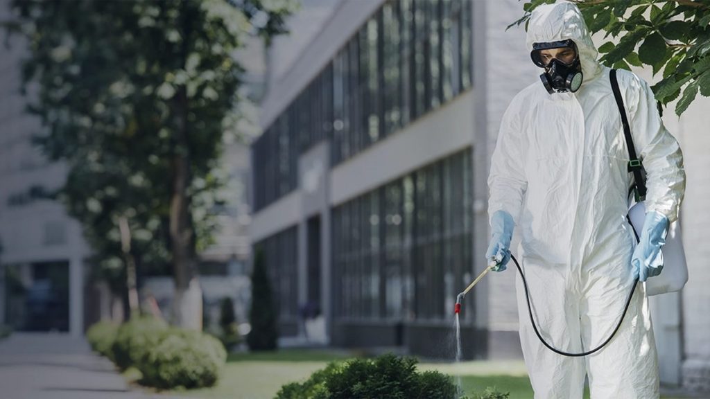 Técnico de controle de pragas em área externa de imóvel comercial.